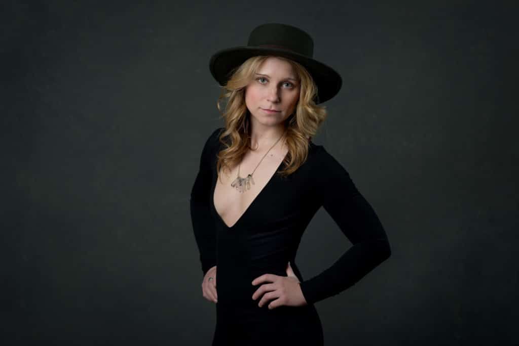 blonde model wearing a v-neck black dress, crystal necklace and wide brimmed hat for a headshot in South Jersey