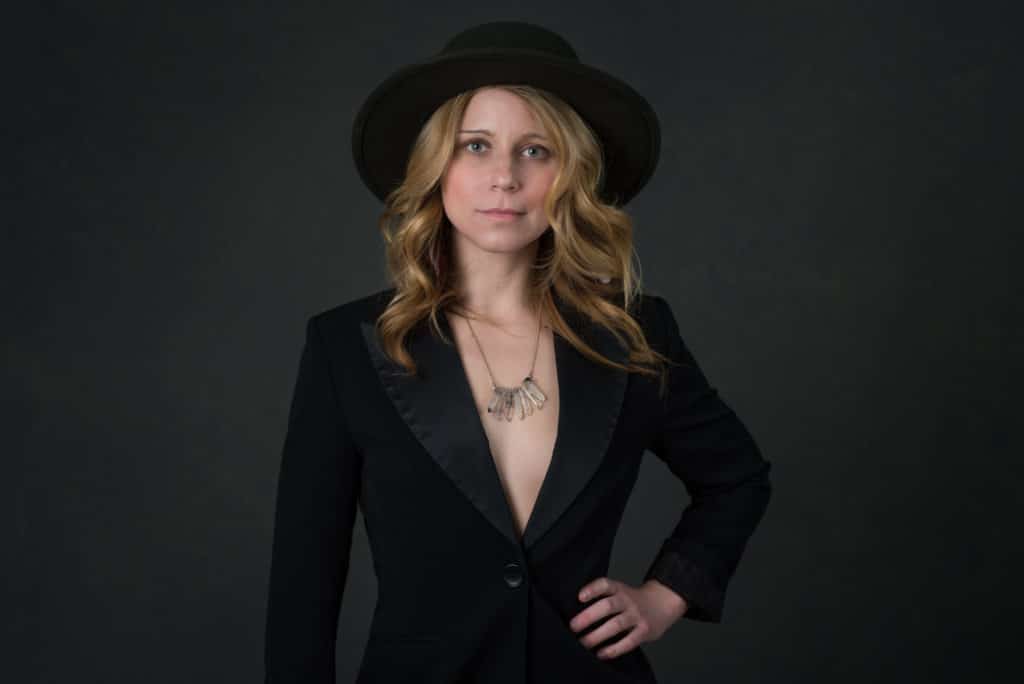 blonde model wearing a hat and tuxedo jacket with crystal necklace on a canvas backdrop in South Jersey photography studio.