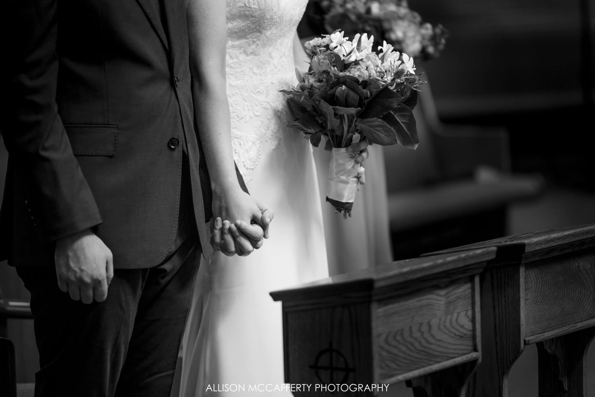 Black and white photo of bride and groom holding hands in church