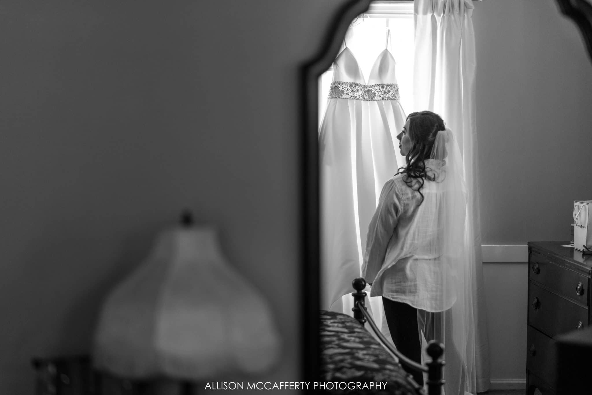 black and white photo of bride looking at her gown in a reflection