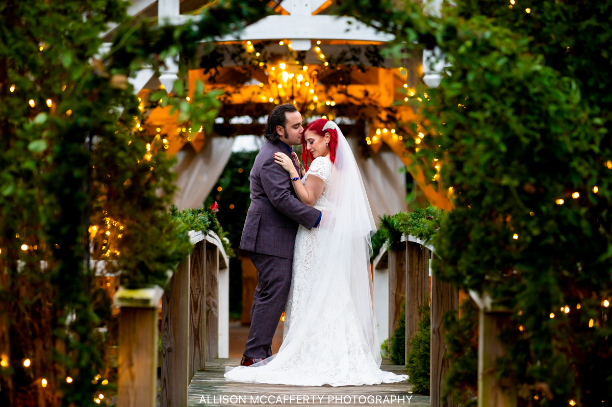 bride and groom standing on a wooden bridge with twinkle lights behind them on the grounds of Abbie Holmes Estate