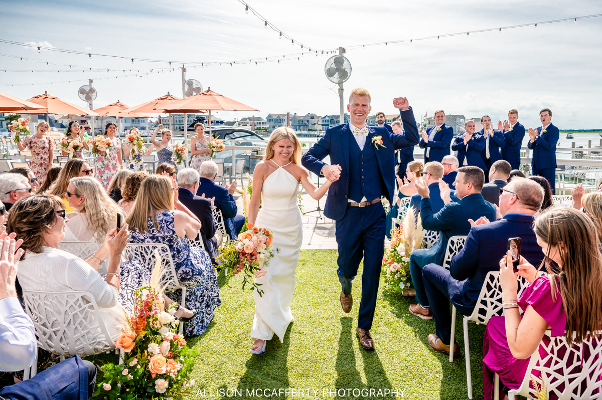 bride and groom holding hands smiling and cheering after their Reeds at Shelter Haven wedding ceremony that overlooked the bay in Stone Harbor NJ