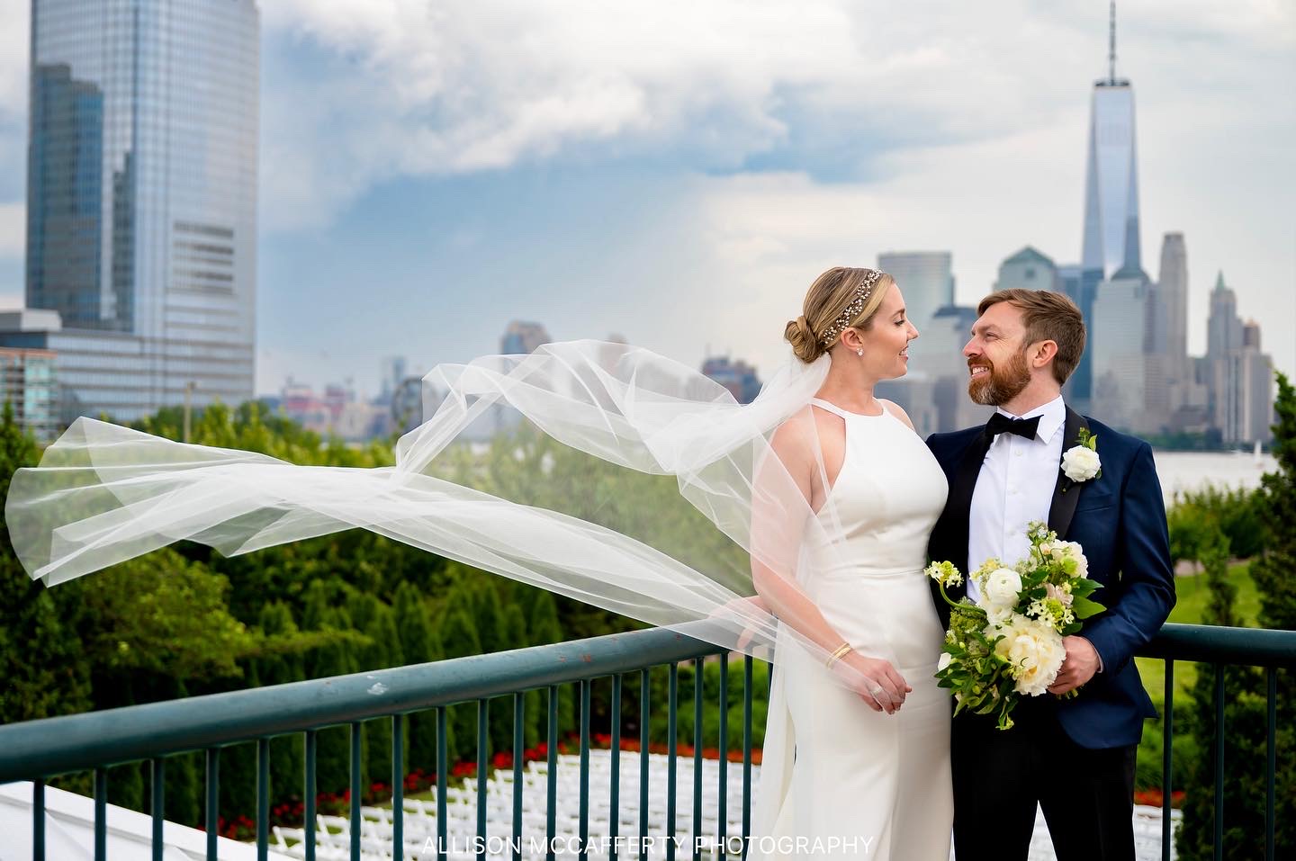 Wedding portrait of a couple standing on the outside patio of Liberty House Restaurant in Jersey City. The bride's long veil is blowing in the wind.
