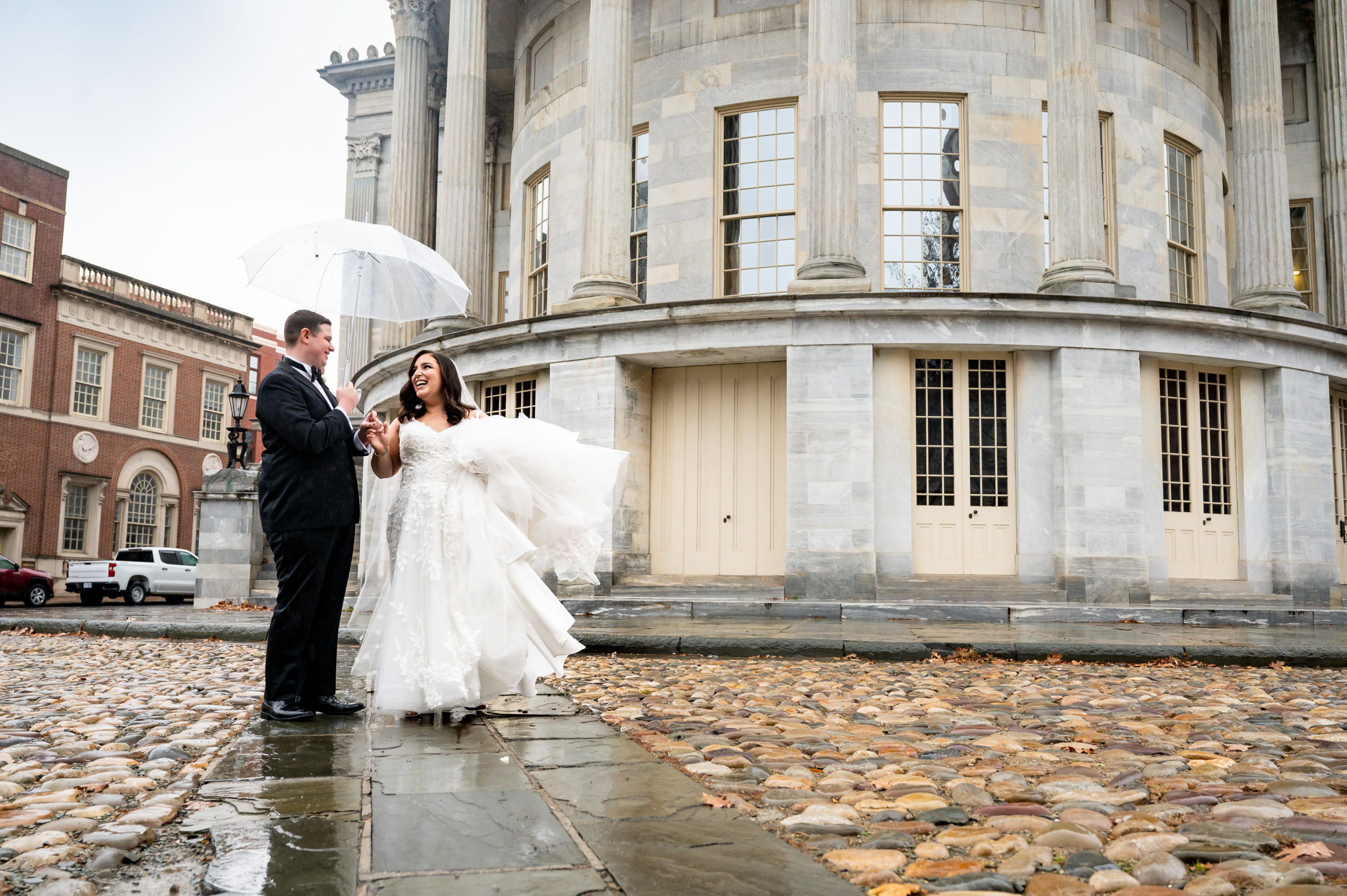 Rainy wedding photo of a couple holding an umbrella in front of Merchant's Exchange Building in Philadelphia PA