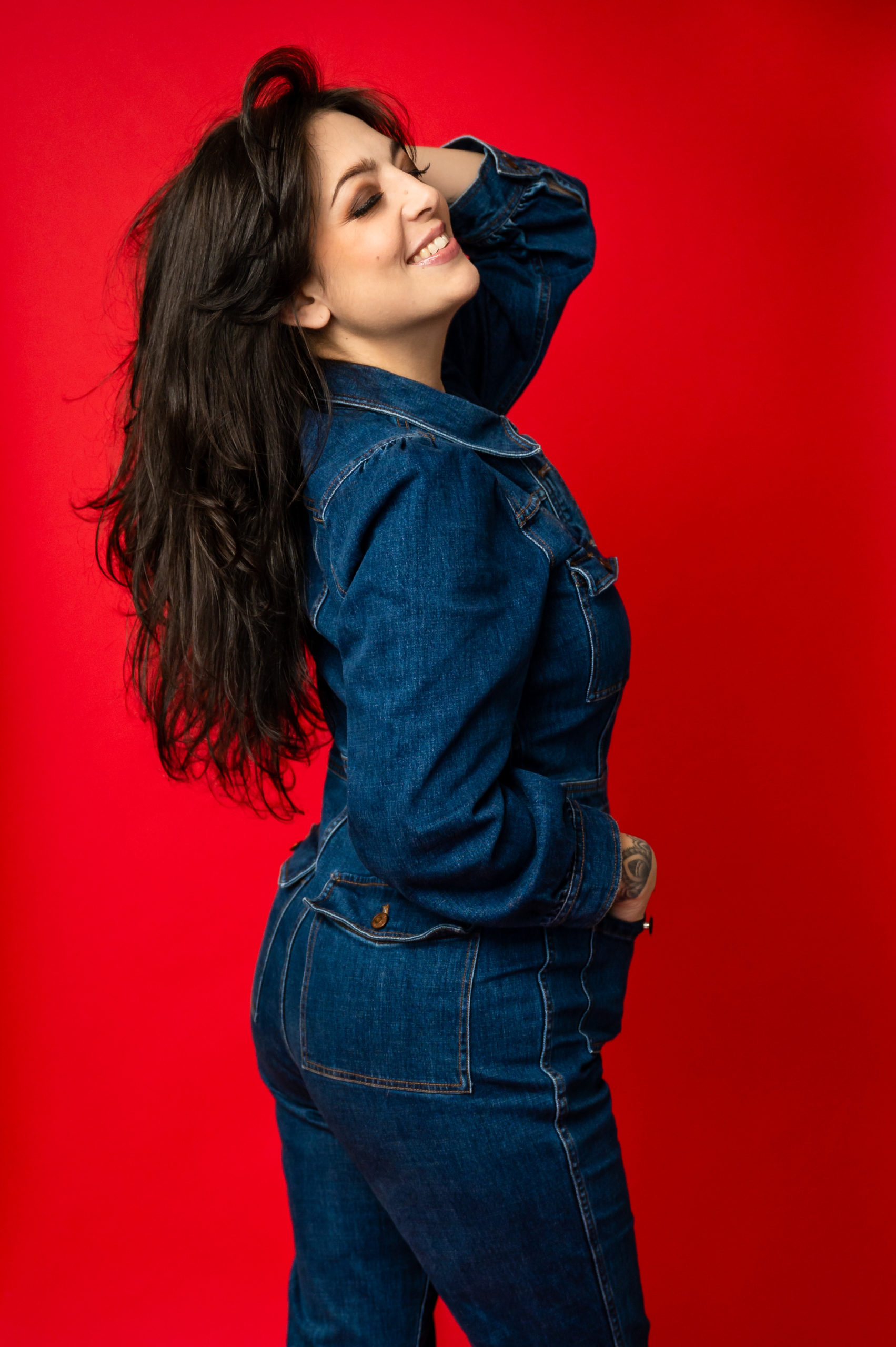 Studio portrait of a woman wearing a jean jumpsuit in front of a red background