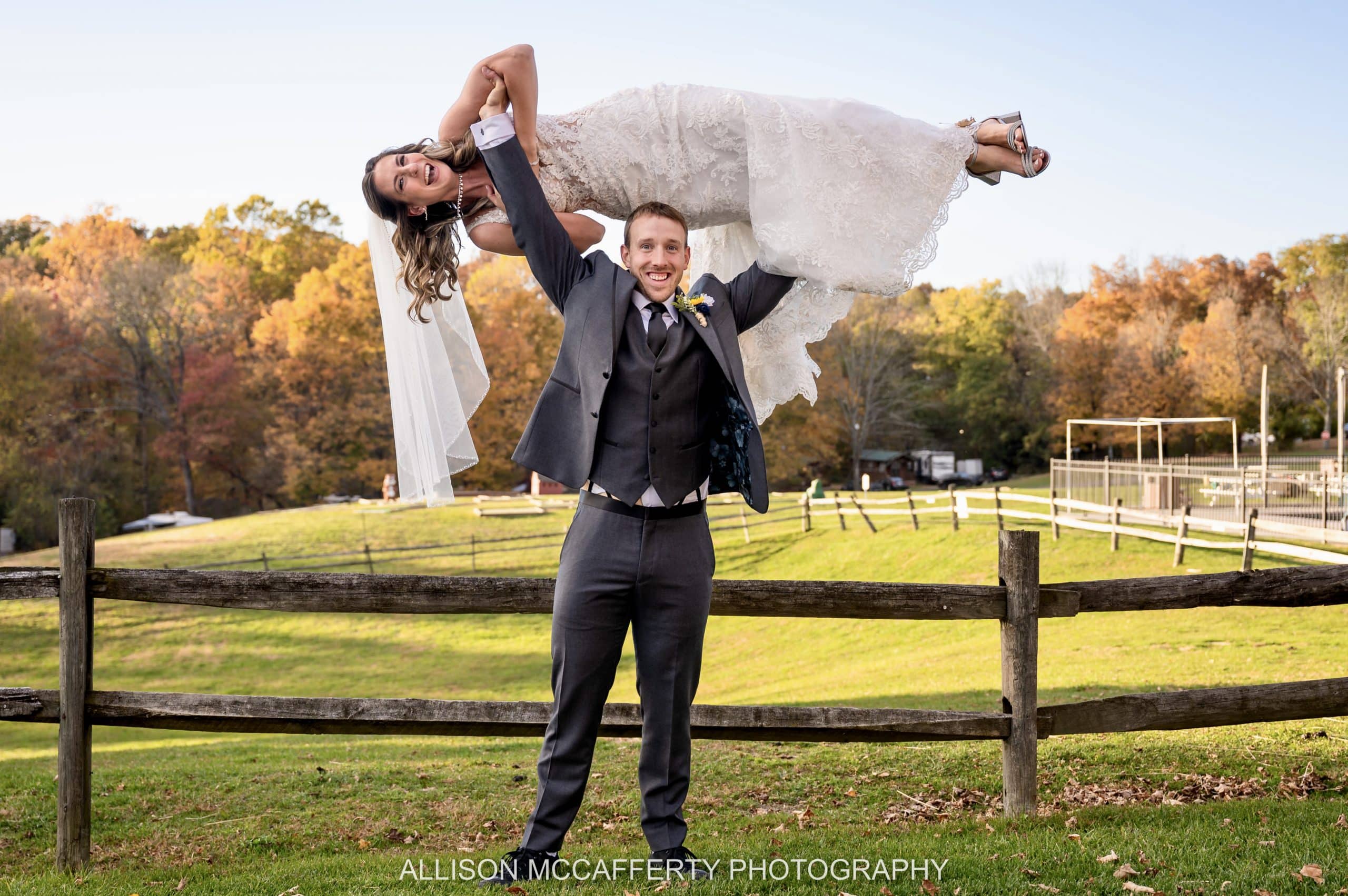 Photo of a man holding his wife over his head in her wedding gown at Triplebrook Campground in Blairstown NJ