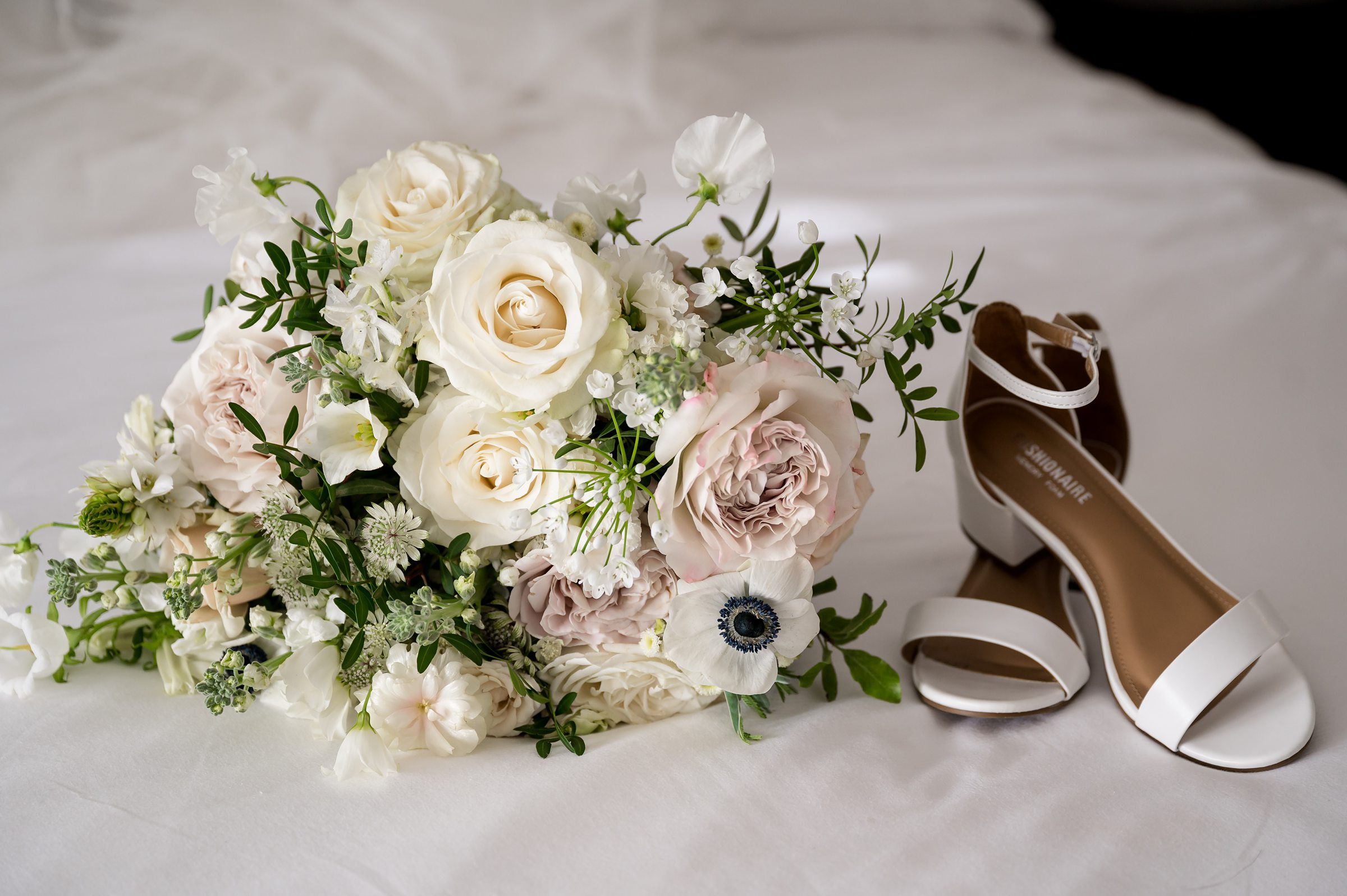 A bouquet of flowers and shoes on a bed, perfect for a Lilah Events wedding.