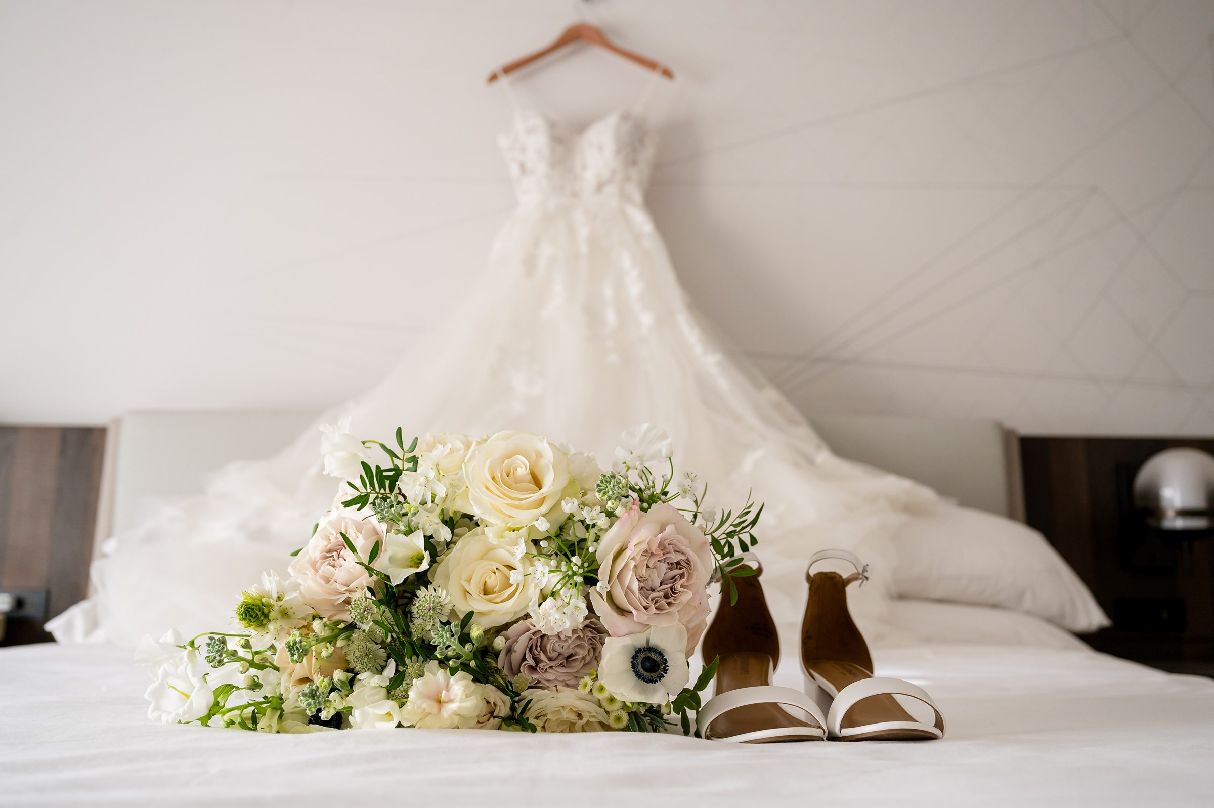 A wedding dress, bouquet, and shoes are elegantly displayed on the bed at a Lilah Events wedding.