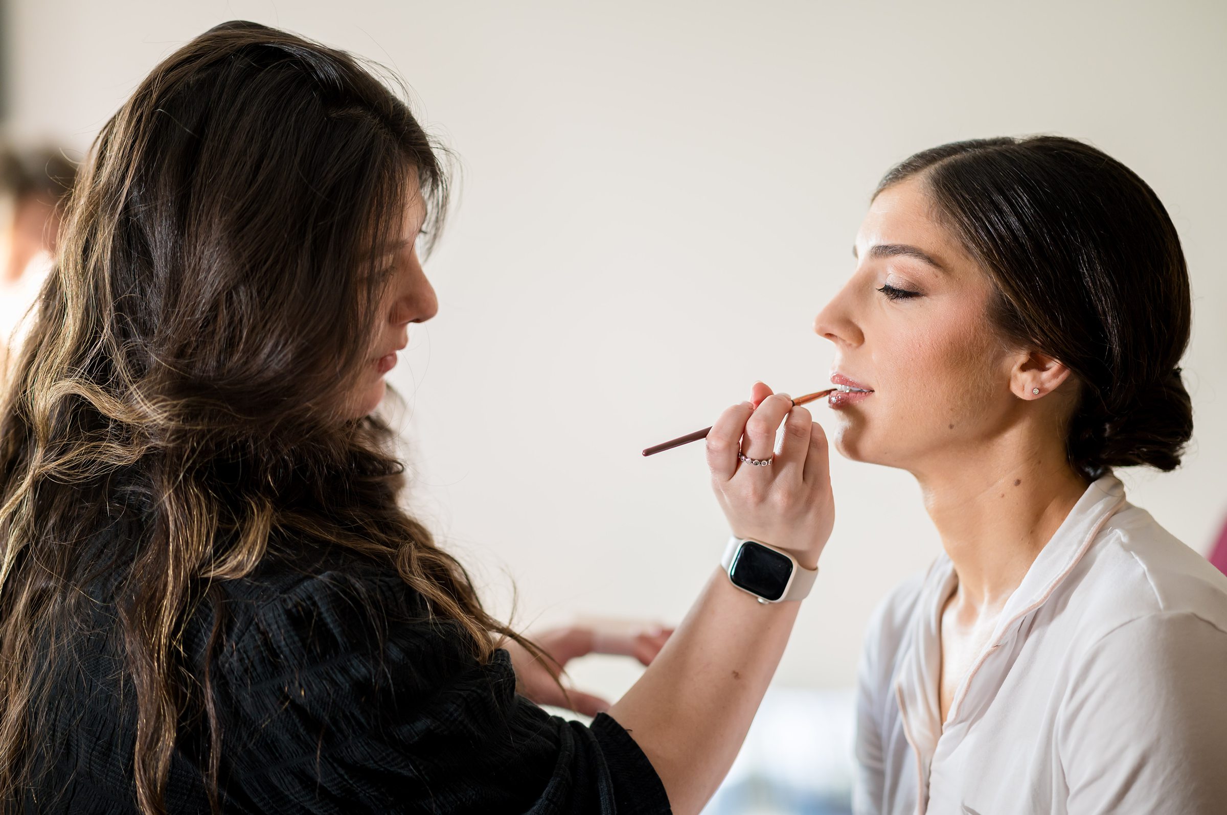 A woman is getting her makeup done by a makeup artist at a Lilah Events wedding.