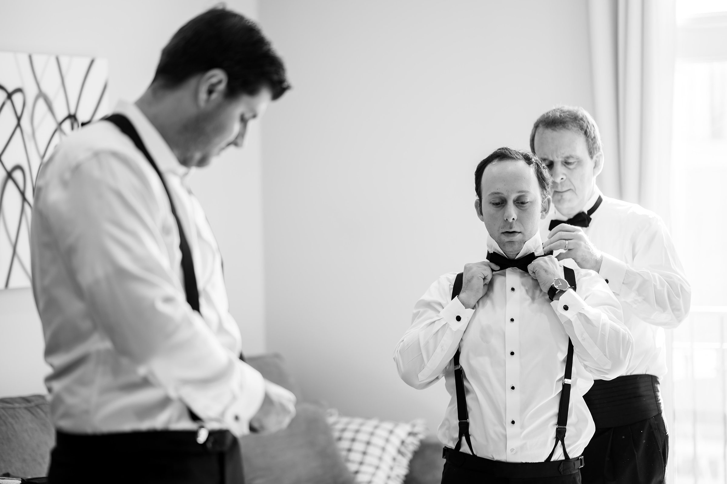A groom is adjusting his suspenders in this charming black and white photo captured by Lilah Events at a wedding.