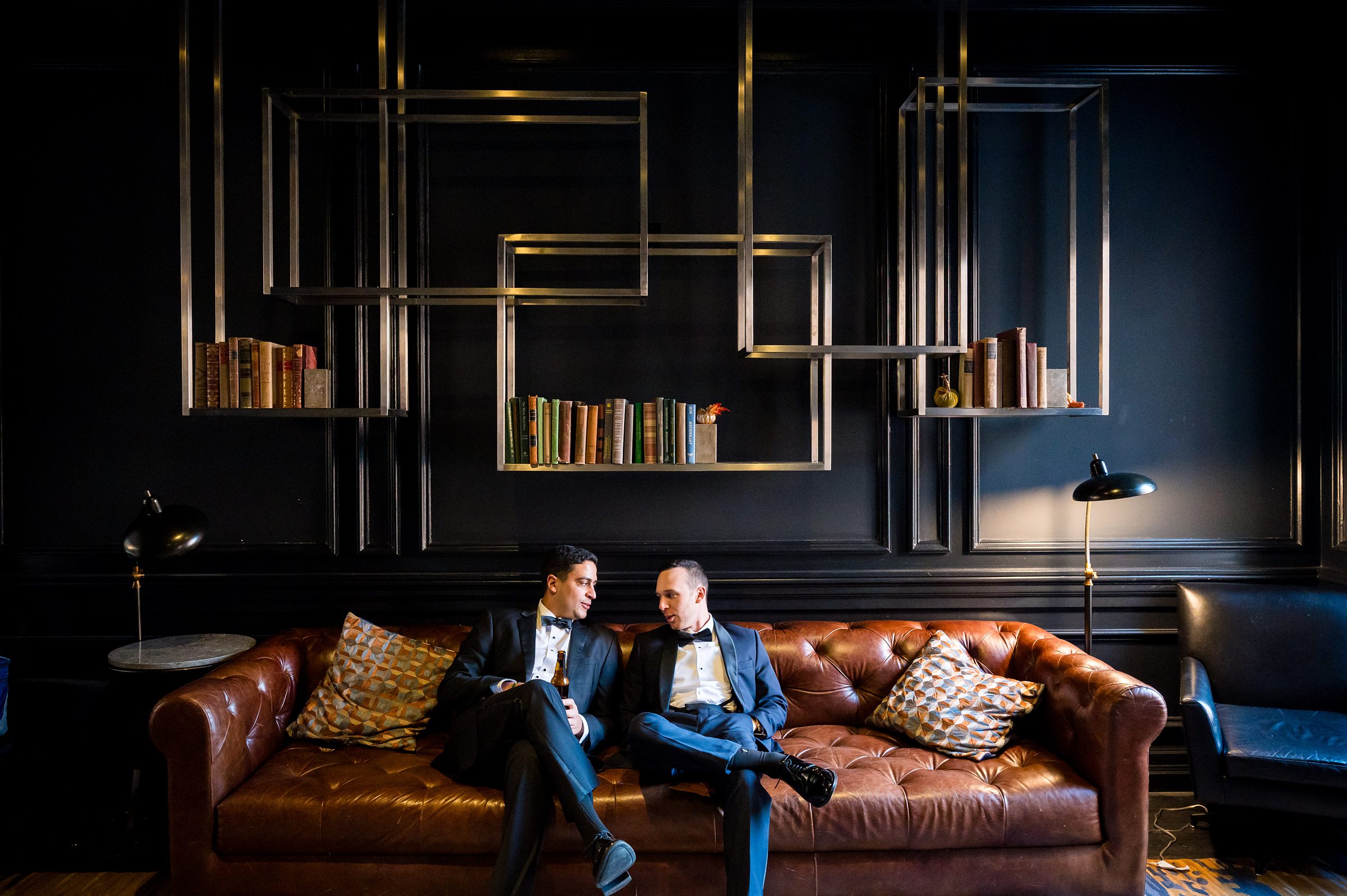 Two men sitting on a leather couch in a dark room during Lilah Events  Wedding.
