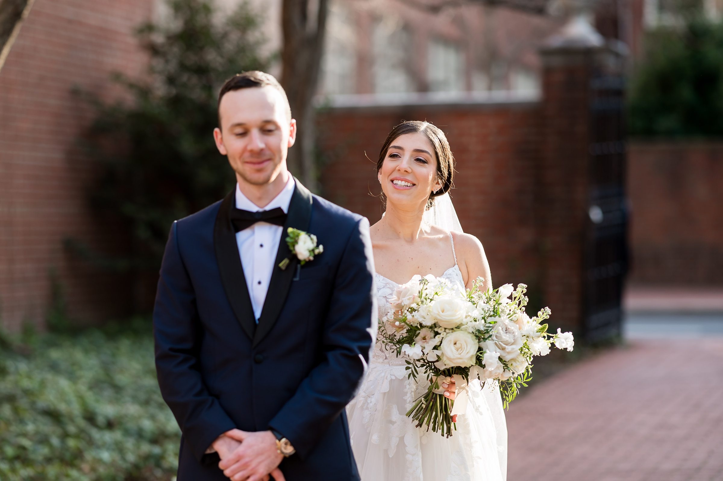 A bride and groom from Lilah Events smile as they walk down a brick walkway at their wedding.
