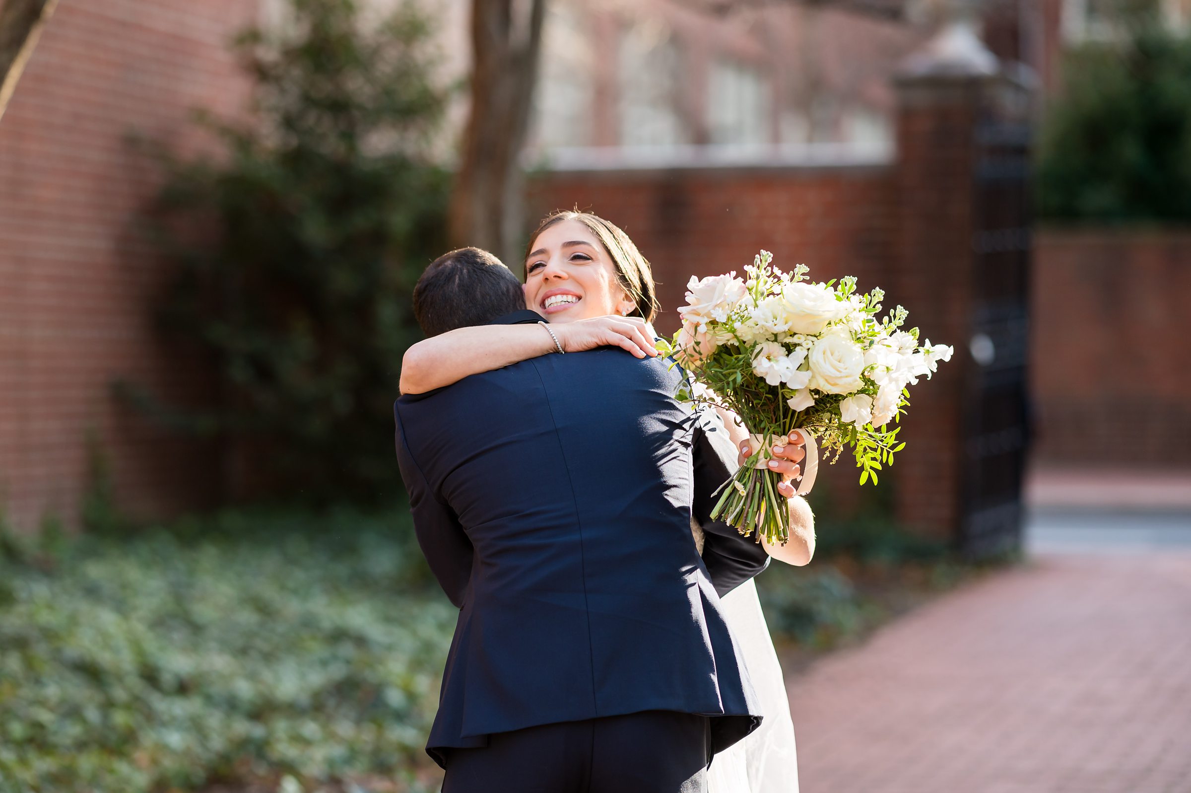 A bride and groom embrace lovingly in front of a brick building.