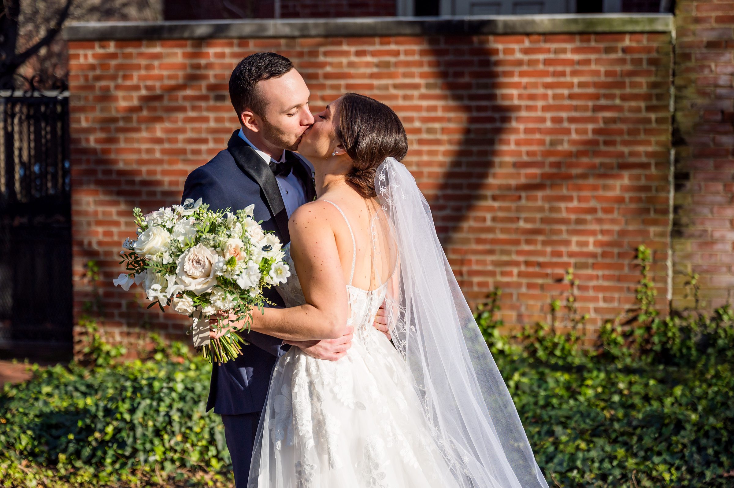 At a Lilah Events wedding, the bride and groom share a kiss in front of a beautiful brick building.