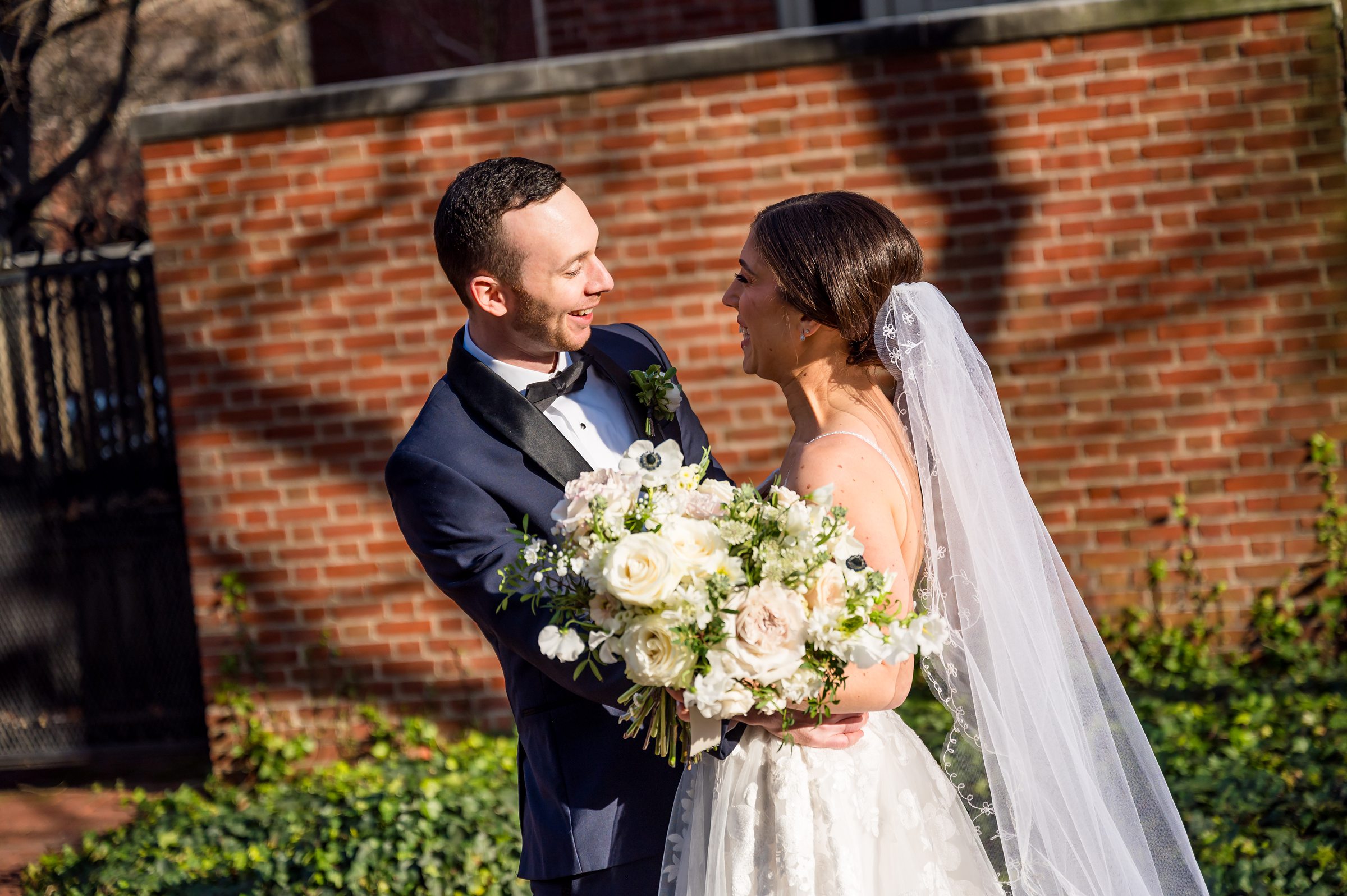 A bride and groom stand gracefully in front of a brick building.