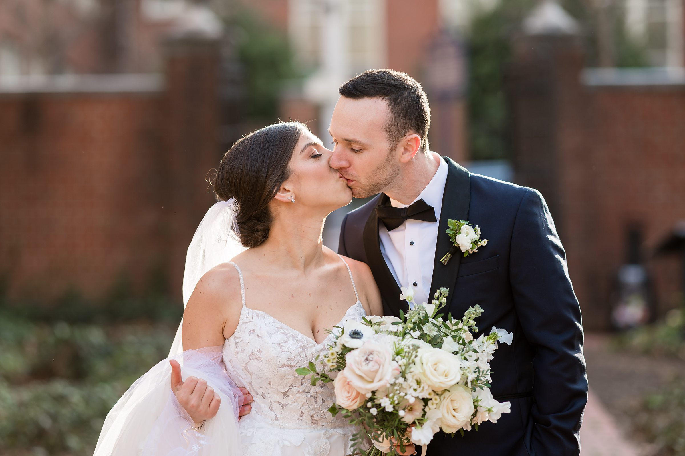At a Lilah Events wedding, the bride and groom share a kiss in front of a brick building.