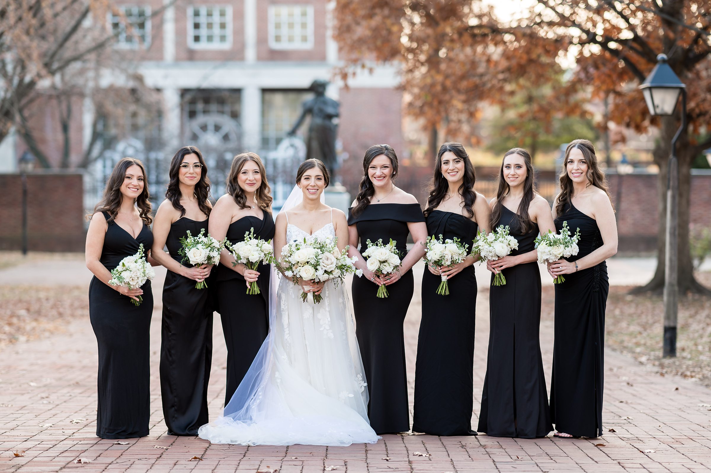 Bridesmaids in black dresses standing in front of a brick walkway at a Lilah Events wedding.