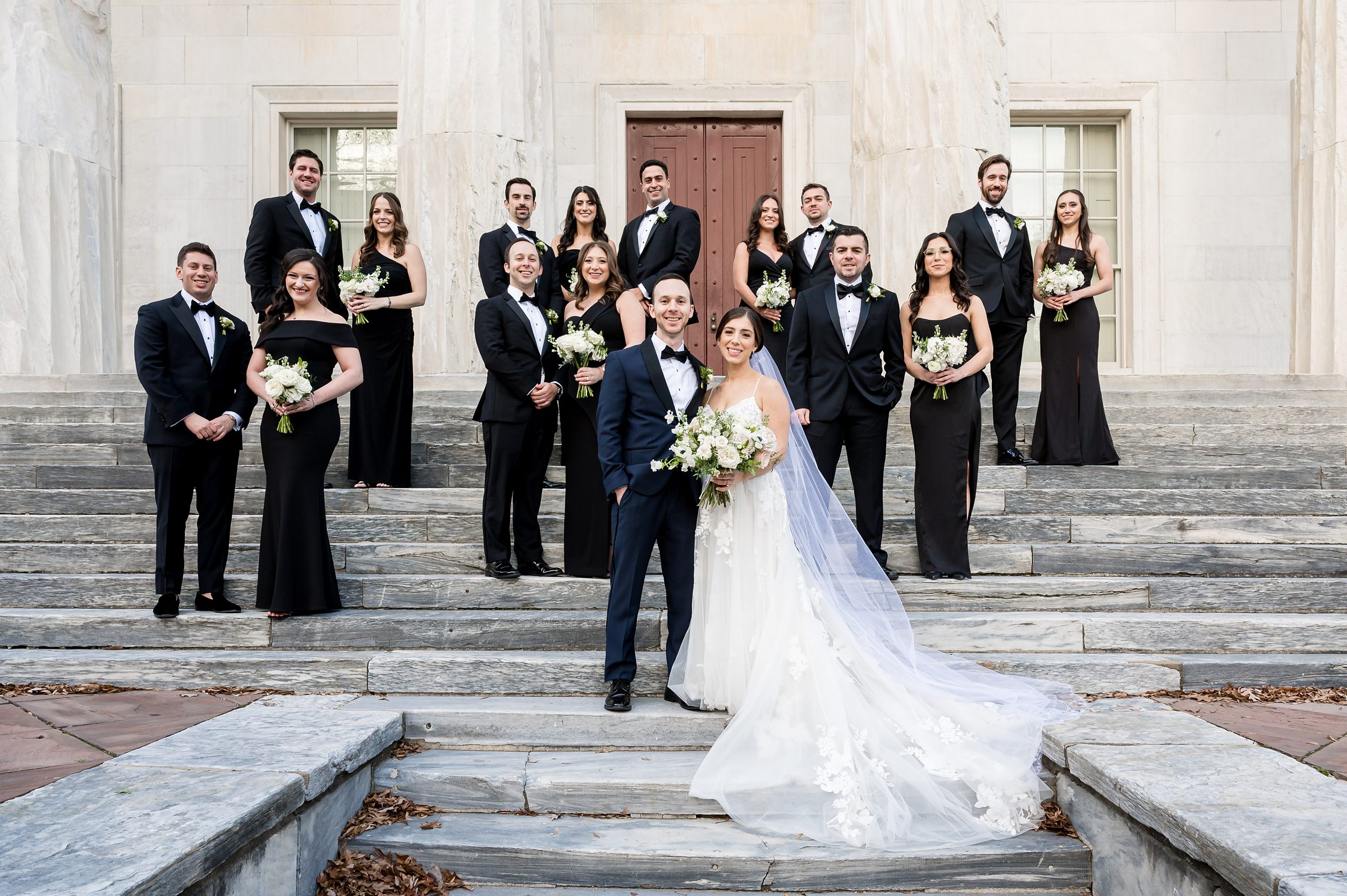 A Wedding party is posing on the steps of a building at Lilah Events.