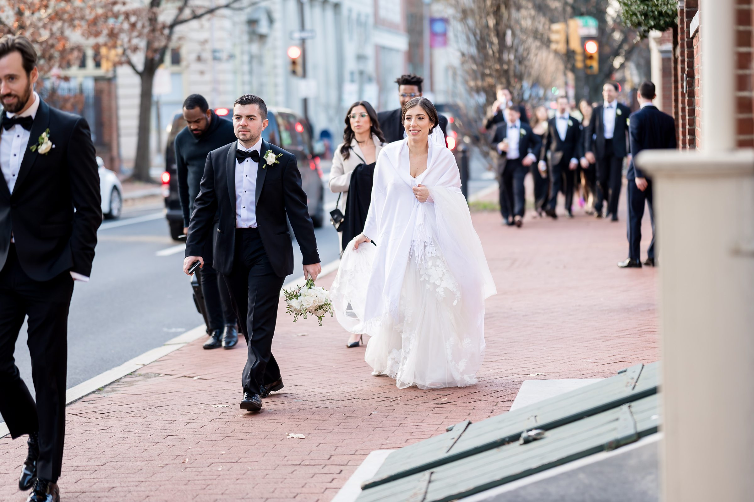 A bride and groom, along with their wedding party, are strolling down the street to celebrate their Lilah Events Wedding.