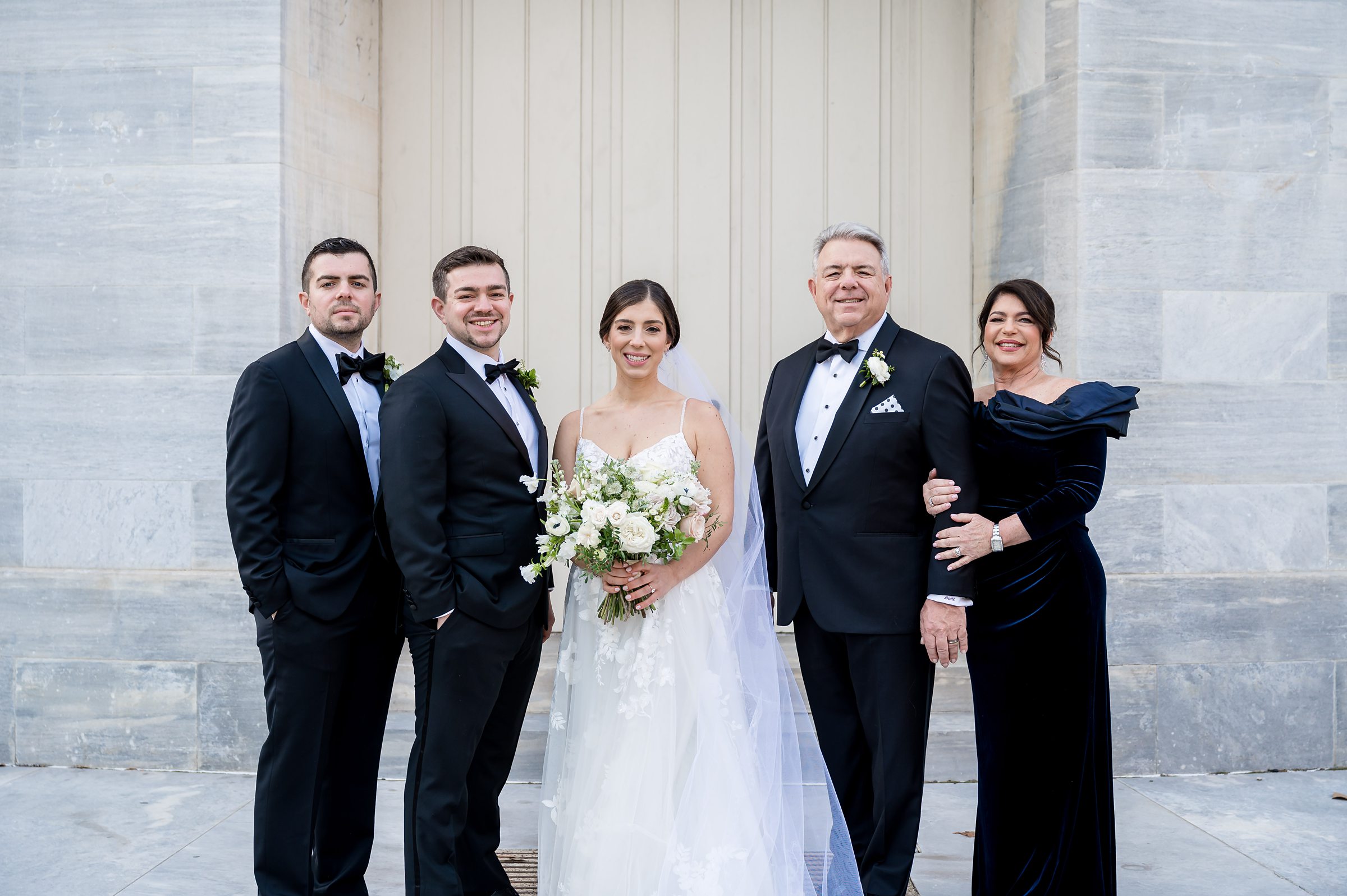 The bride and her family take a photo in front of a building during their Lilah Events wedding.