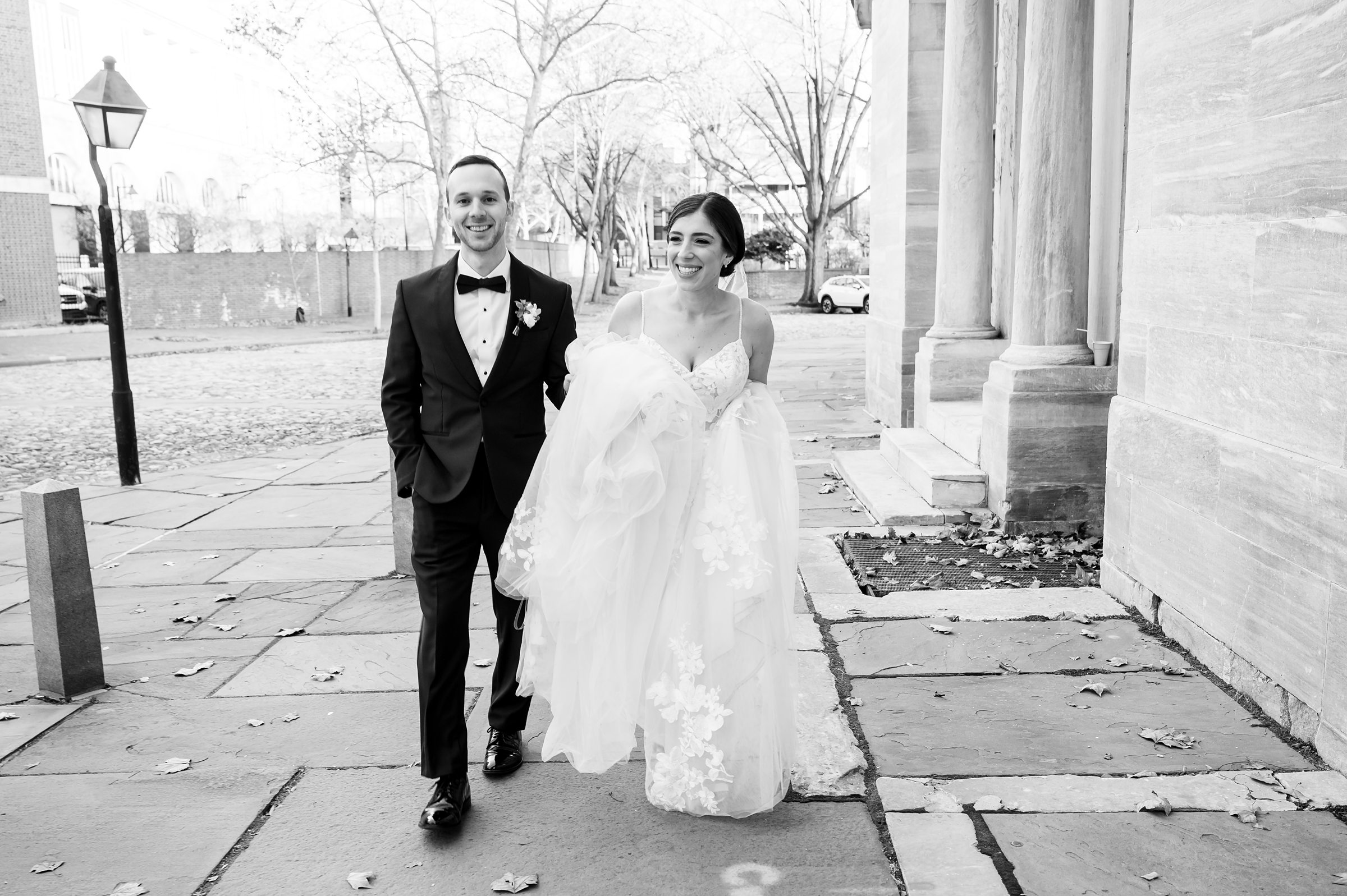 A black and white photo of a bride and groom walking in front of a building at a Lilah Events wedding.