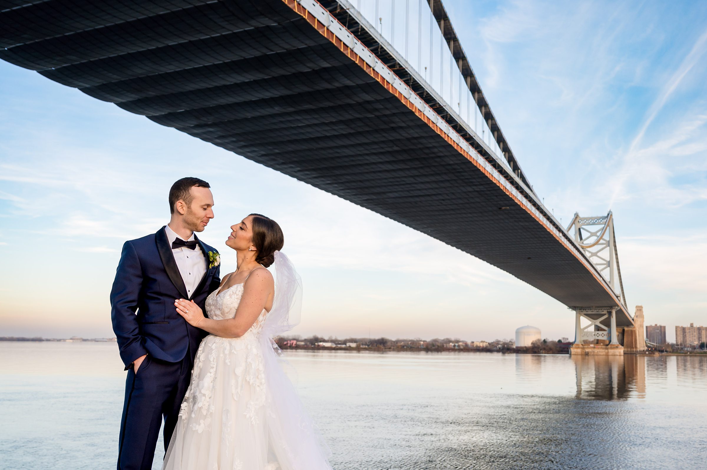 A bride and groom standing under a bridge at their Lilah wedding.