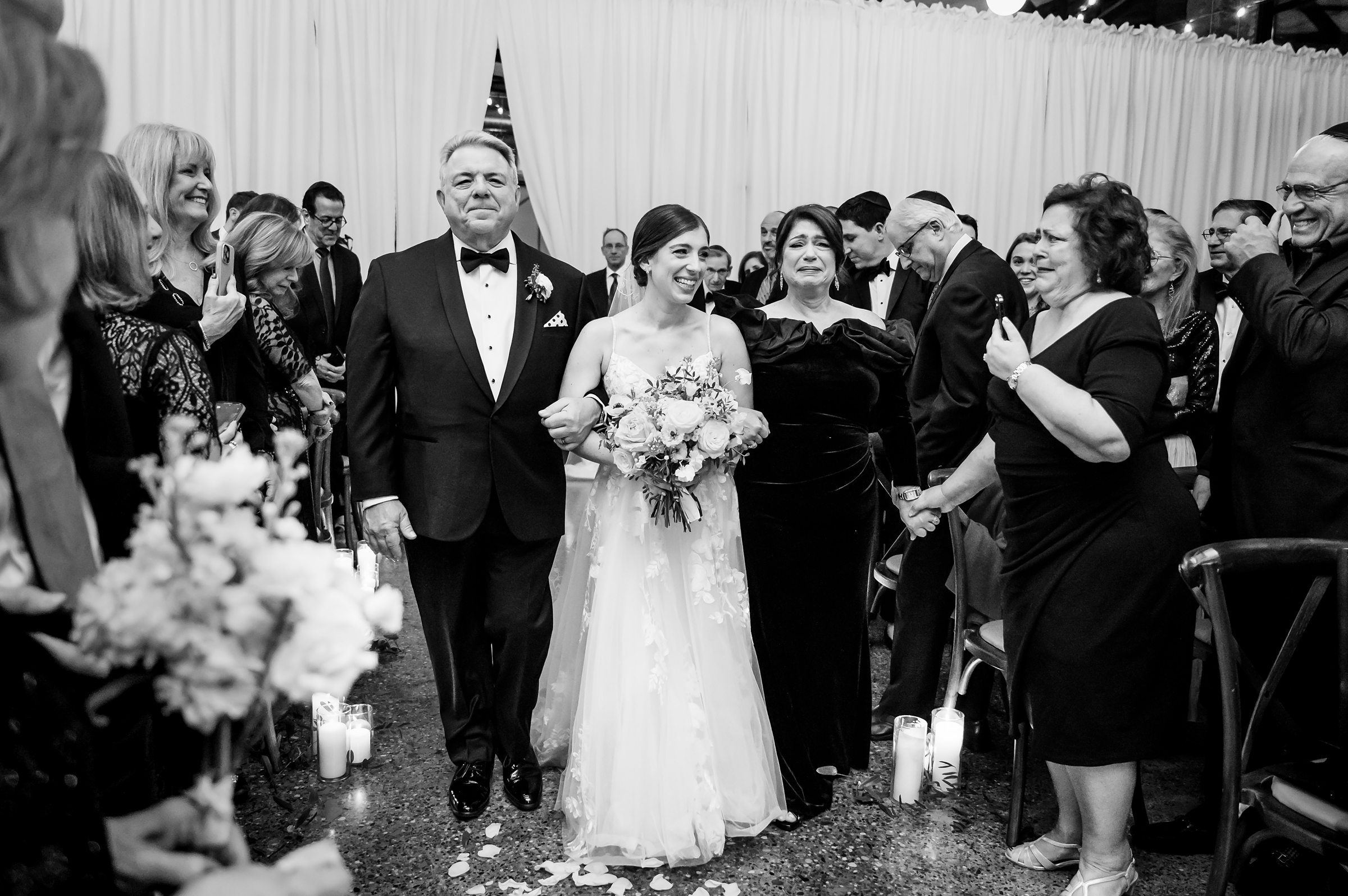 A black and white photo of the bride and her family walking down the aisle at a Lilah Events wedding.