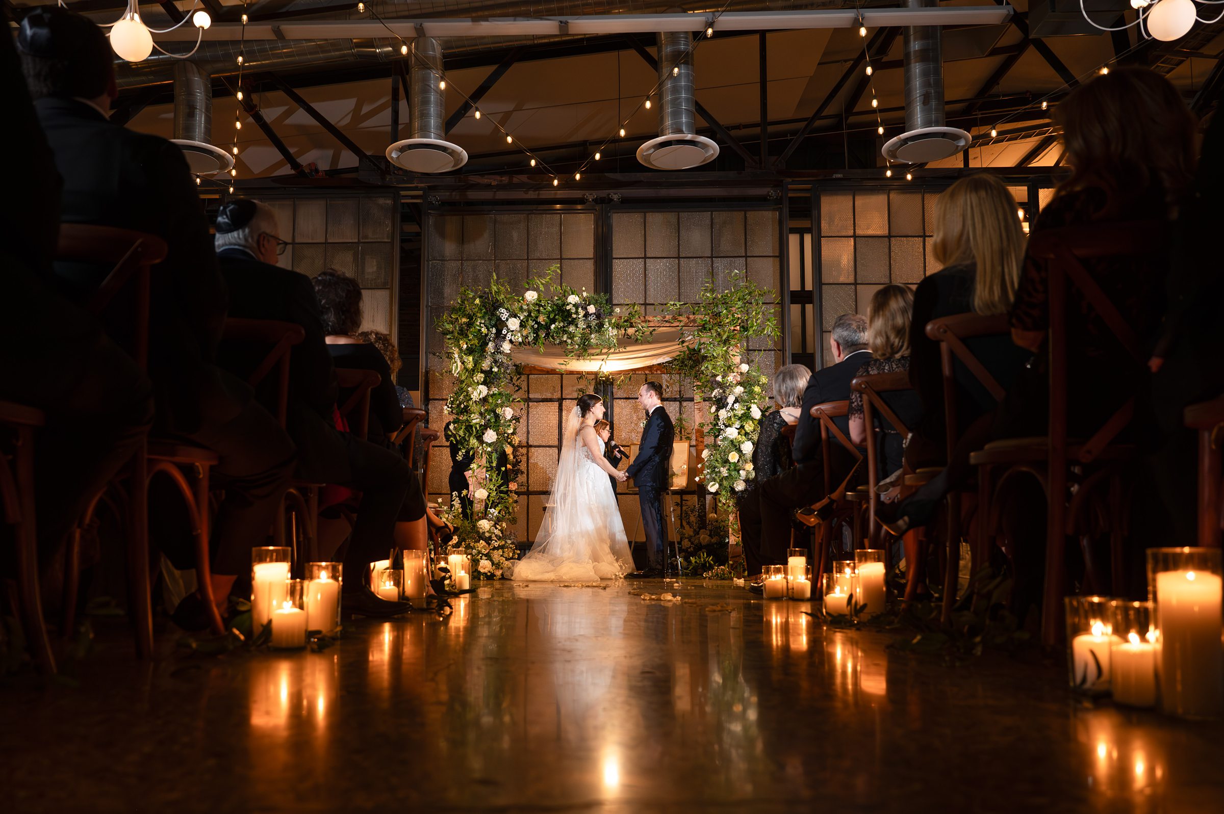 A bride and groom walk down the aisle at a Lilah Events wedding, with candles in the background.