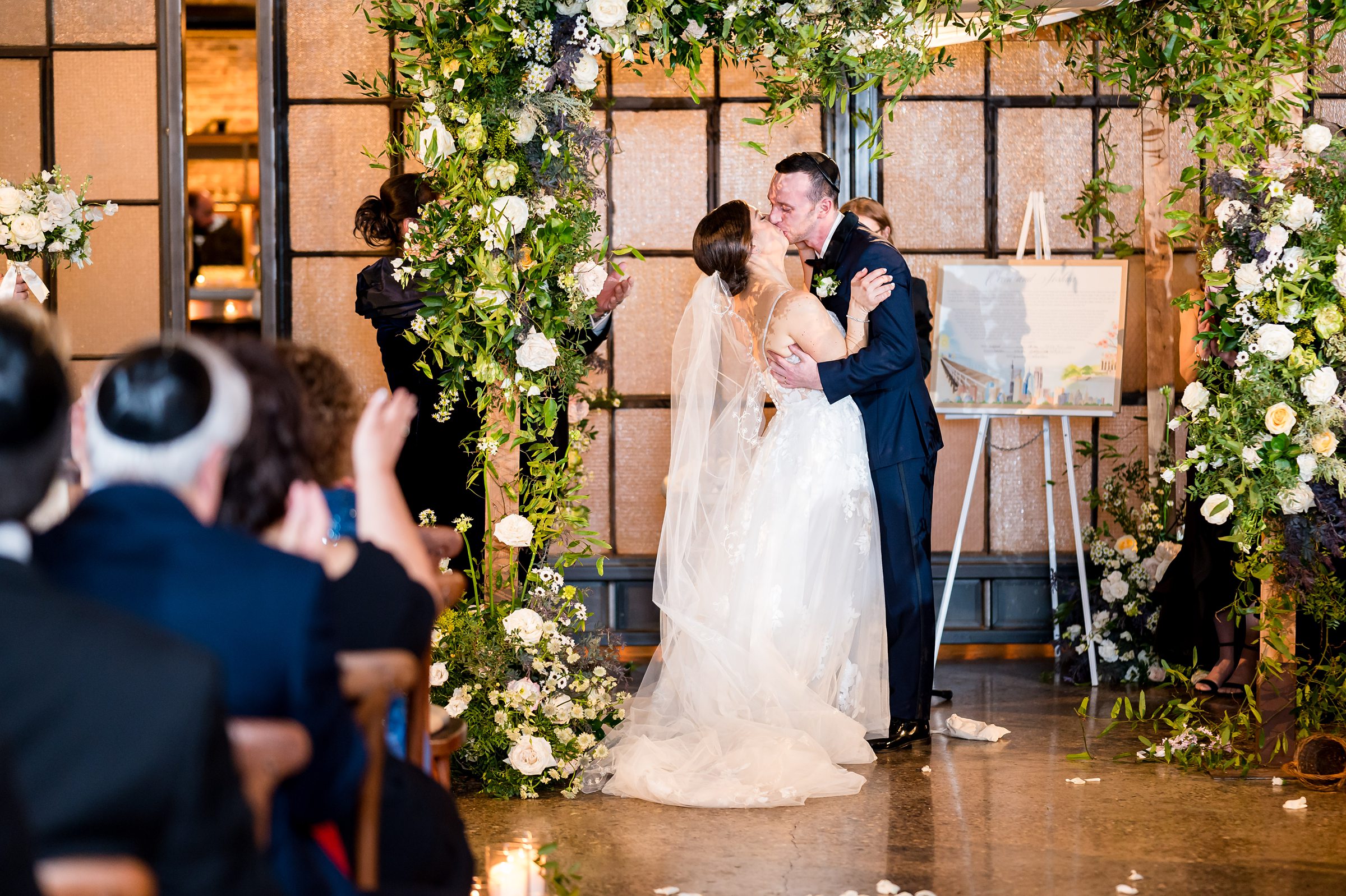At a Wedding ceremony planned by Lilah Events, the bride and groom share a kiss under a floral arch.