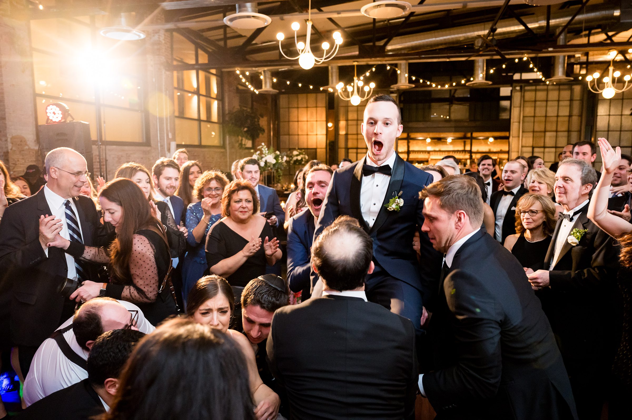 At a Lilah Events wedding, a man in a tuxedo is lifted up by a crowd of people.