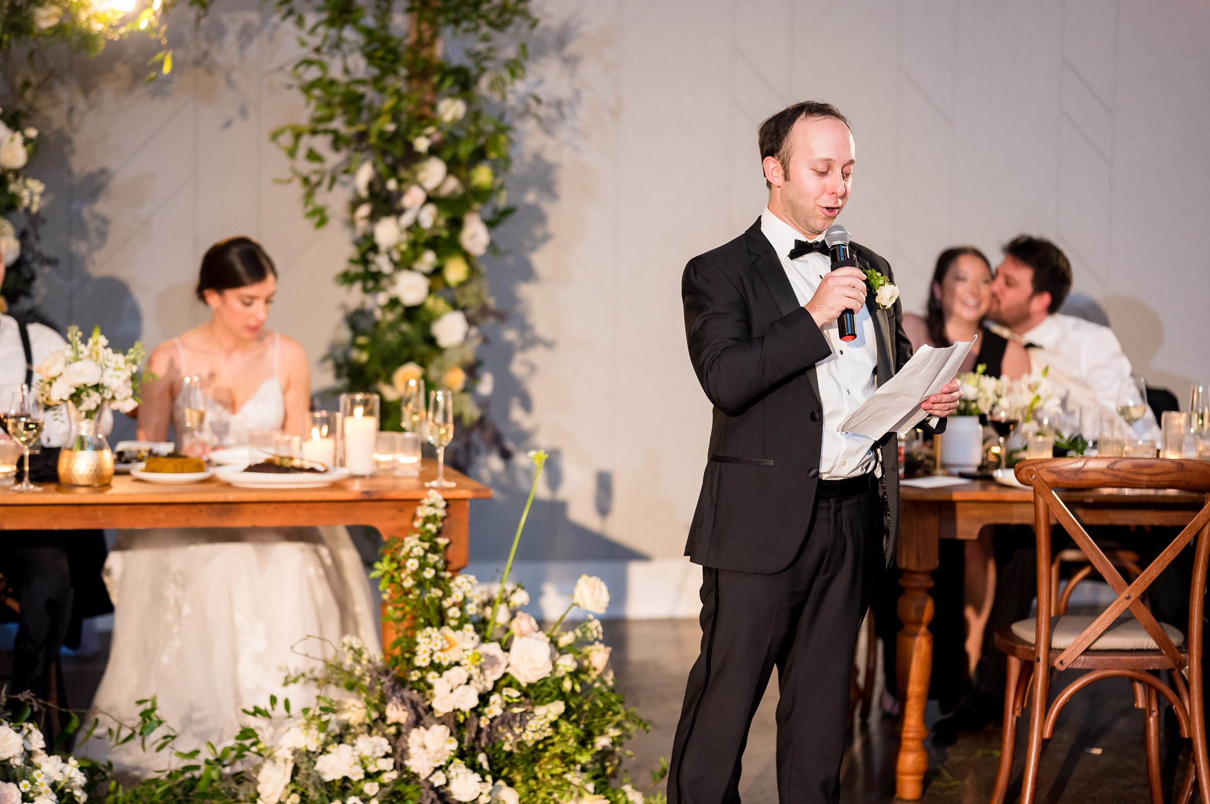 A man in a tuxedo giving a heartfelt speech at a Lilah wedding reception.