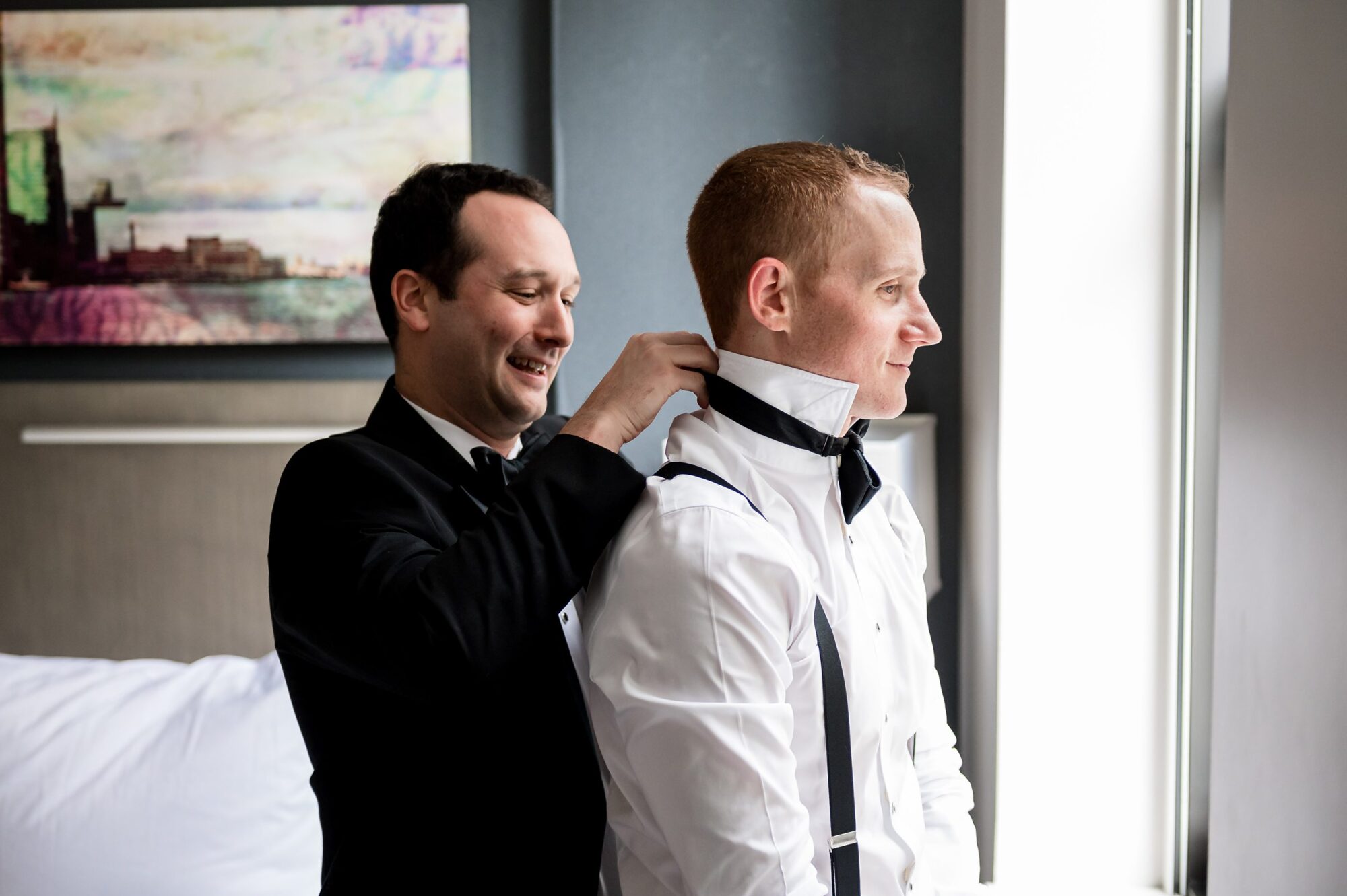 A man putting on a tuxedo in a hotel room.