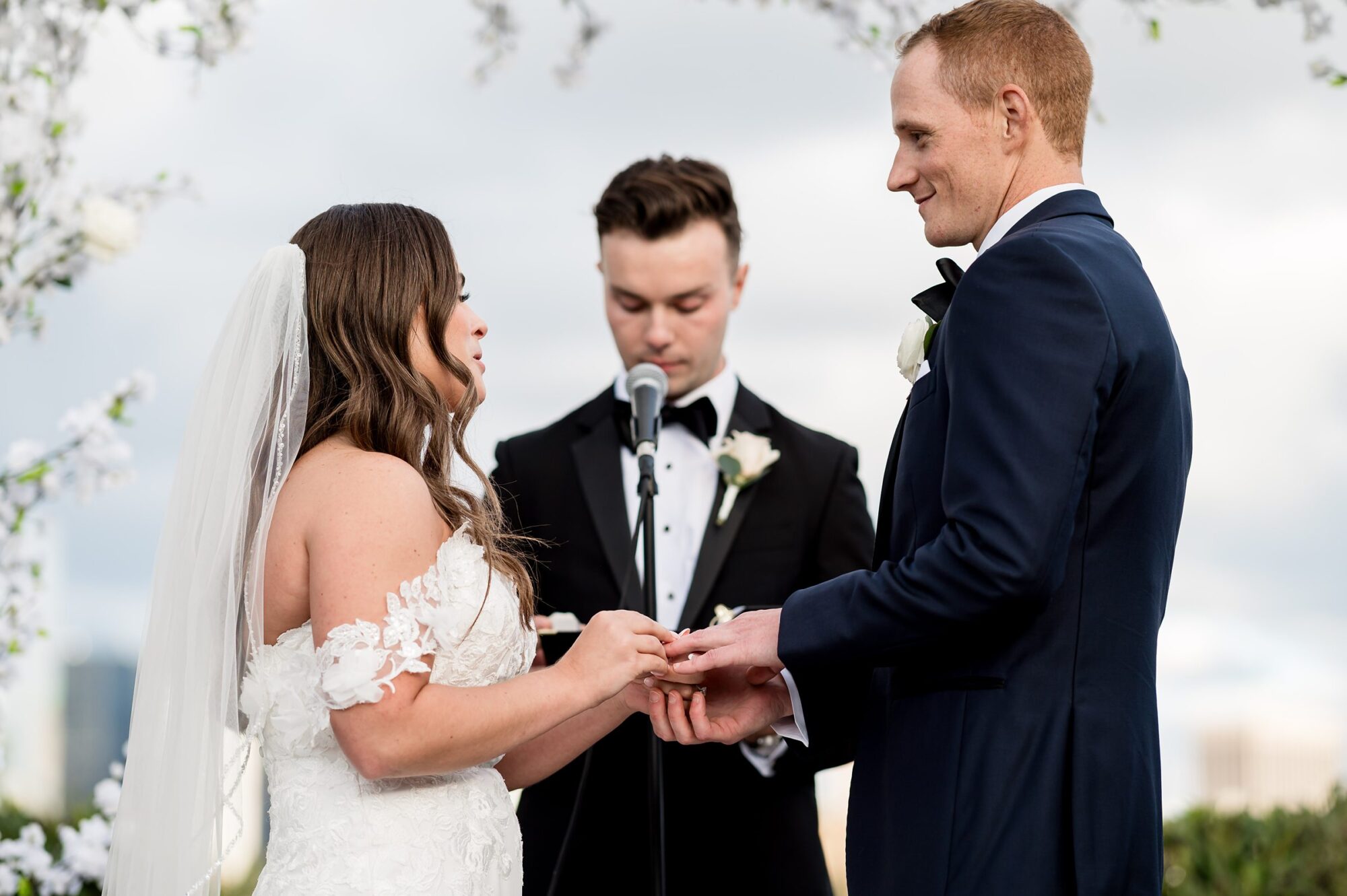 A bride and groom exchange their wedding rings at an outdoor wedding ceremony.