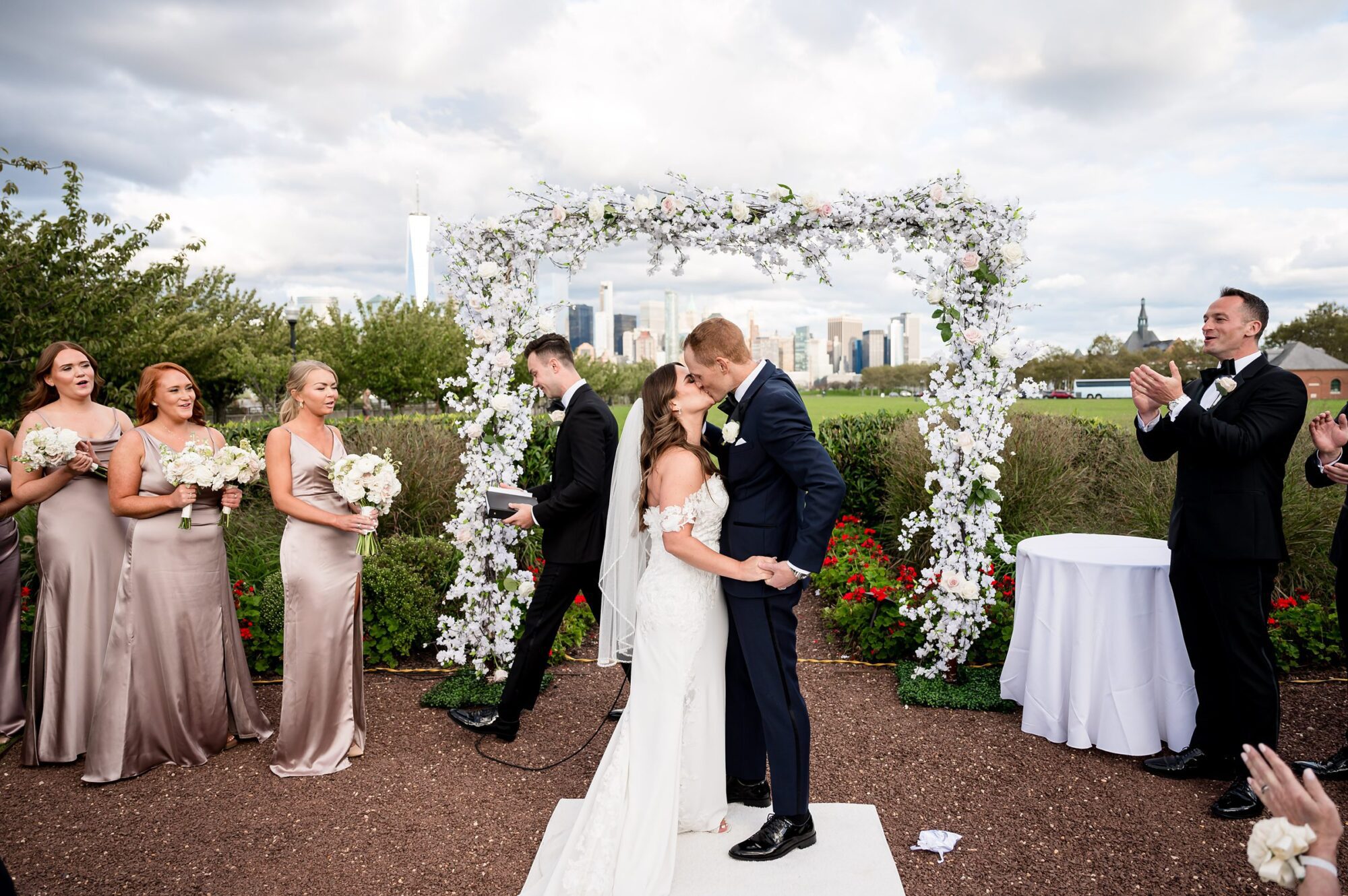 A bride and groom kissing under an arch in front of a city skyline.