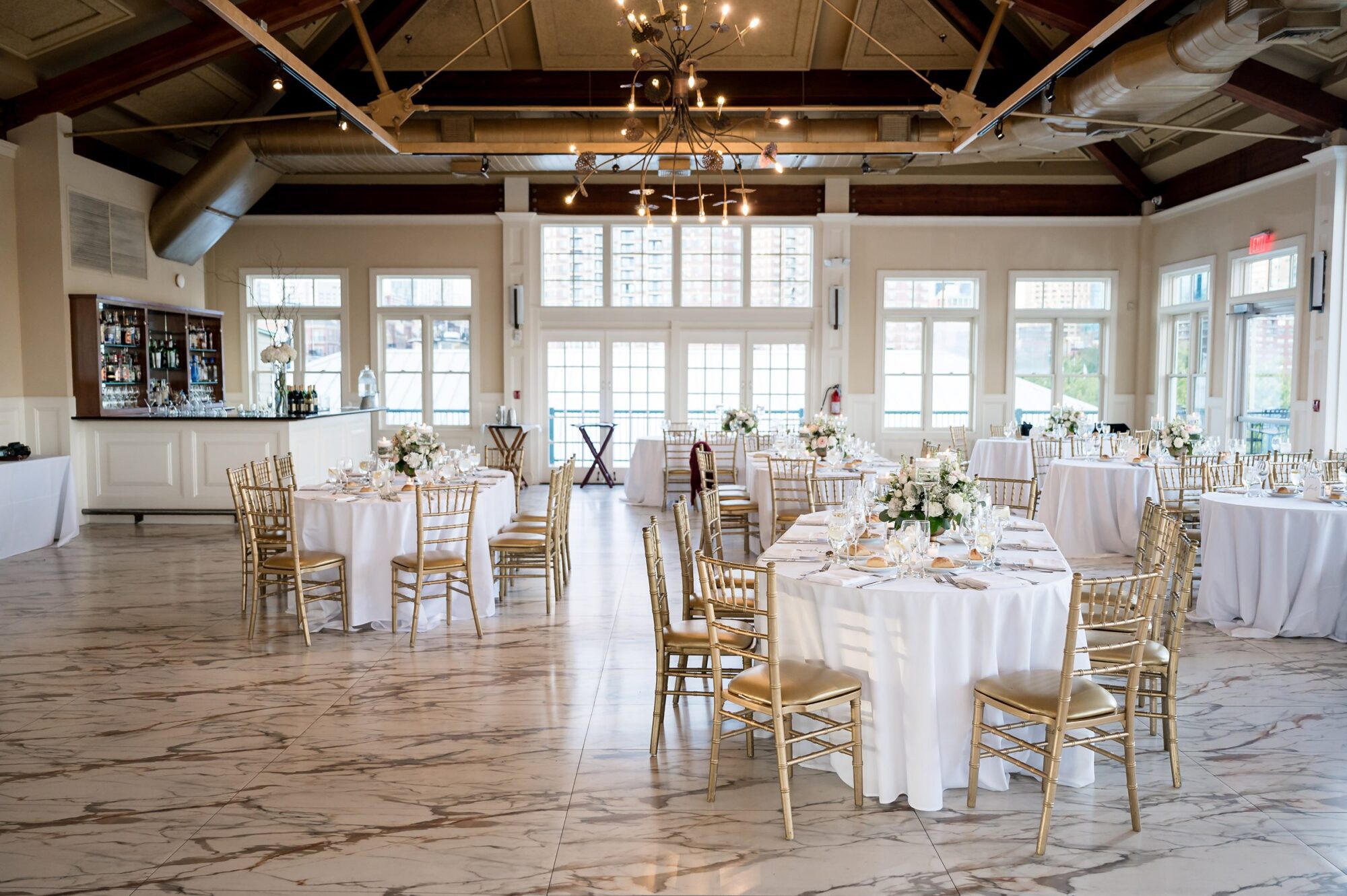A wedding reception set up in a large room with white tables and chairs at Liberty House in Jersey City.