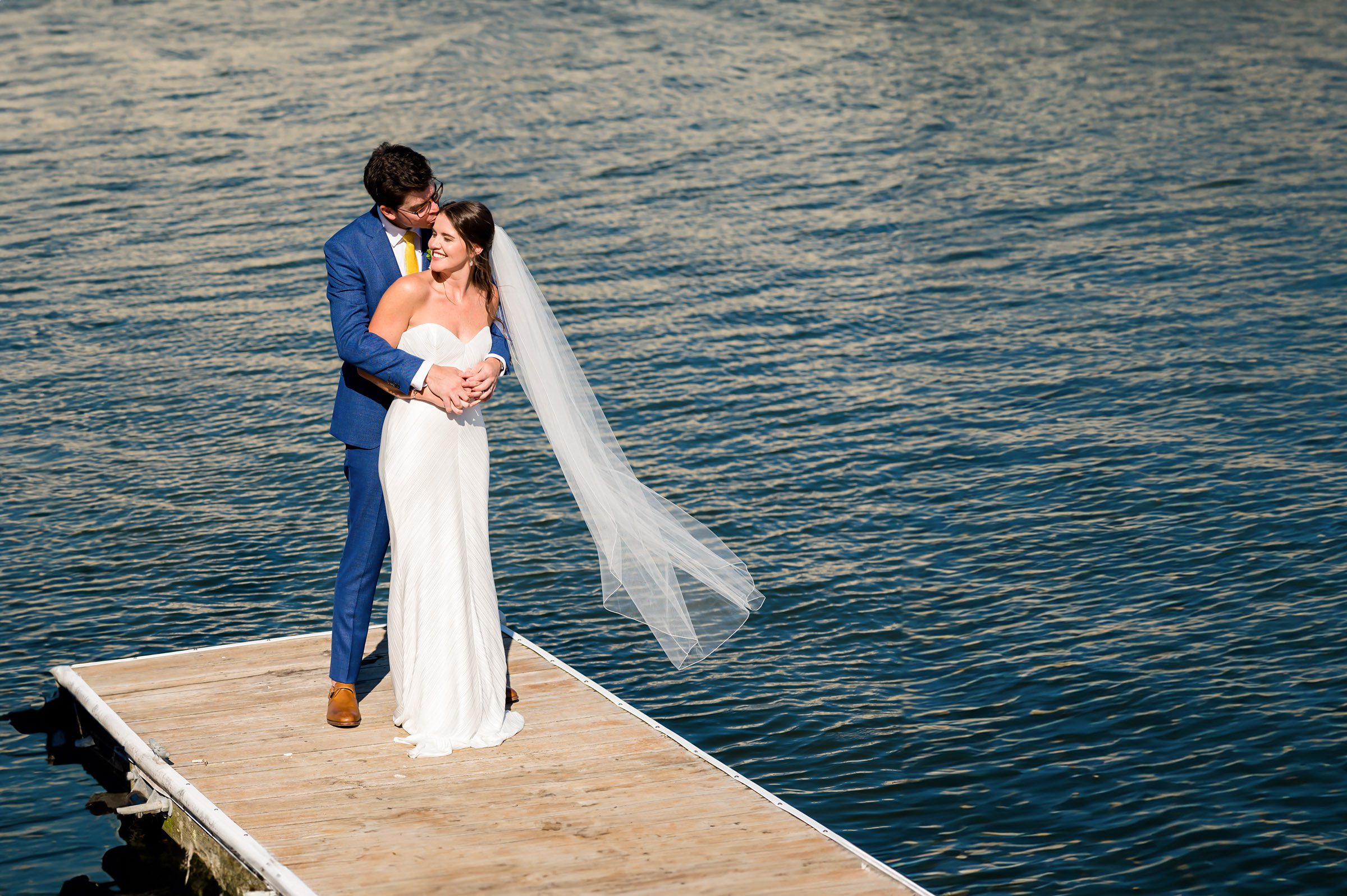 Newlyweds embracing on a wooden dock over tranquil water after their wedding in Stone Harbor NJ before going to their wedding reception at ICONA Windrift