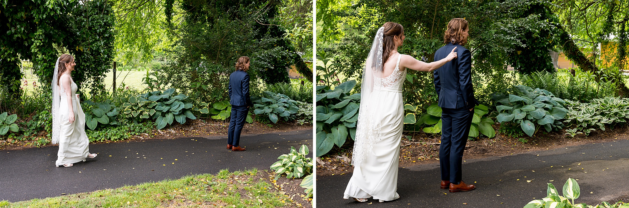 A bride in a white dress and veil walks towards a groom in a navy suit; she taps him on the shoulder in a garden setting.