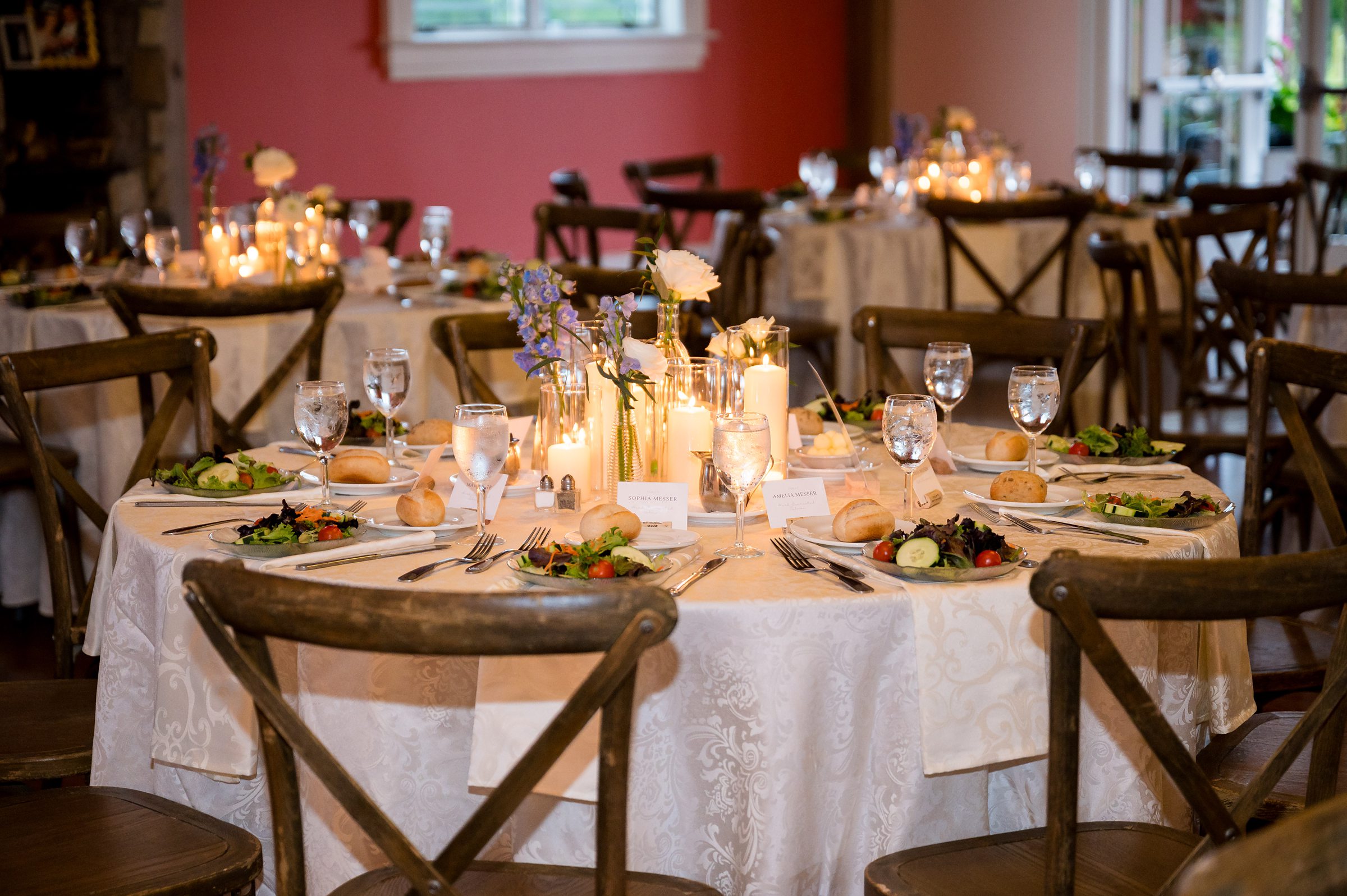Willow Creek Winery Wedding with elegantly set tables with white tablecloths, candles, glasses, and plates of salad in a warmly lit dining area.