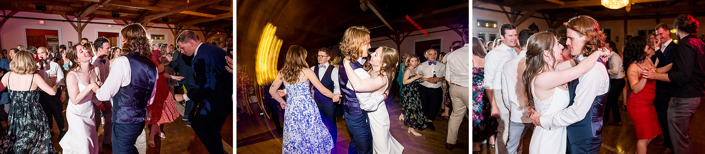 A bride and groom dance among guests at a reception. The bride wears a white dress, and the groom wears a suit with a blue vest. The setting features a wooden ceiling with lights and decor.